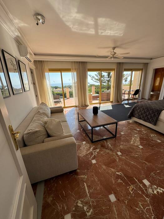 Bright suite living area with a beige sofa and balcony overlooking the sea